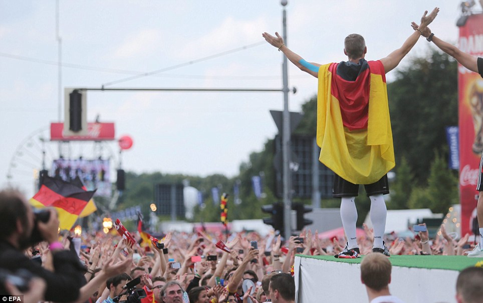 The messiah: A battered and bruised Schweinsteiger gees the crowds up even further draped in a Germany flag on the edge of the platform