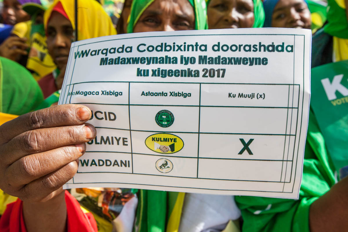 A woman holds up a campaign leaflet in the form of a polling card at a Kulmiye party rally in Hargeisa. Polling cards will include the party symbols to cater for voters that are illiterate. [Kate Stanworth/Saferworld/Al Jazeera]