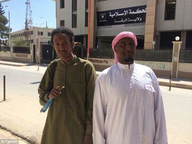 Taymullah al Somali poses with an unidentified militant outside a sharia law court in the Syrian city of Raqqa. The building is adorned with the black jihadist flags symbolic of ISIS' reign of terror in the Middle East