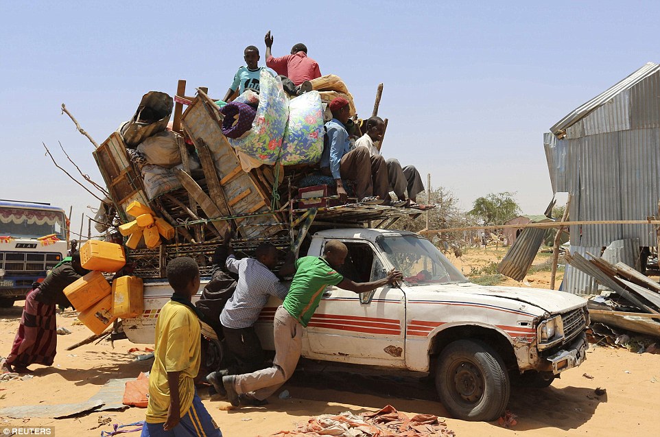 Displaced Somali families help push a battered pick-up truck carrying personal belongings from the camp