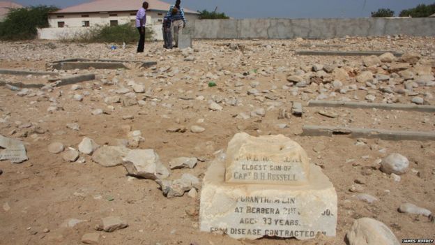 A few fragments of headstones with chipped names and dates amid rocks and sand in Berbera's British cemetery