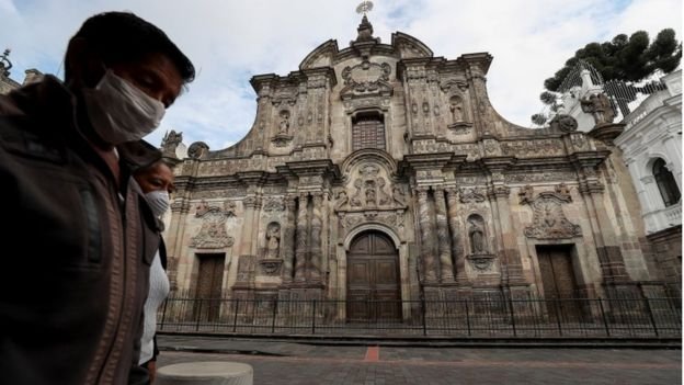 Women with face masks walk by a church in Ecuador