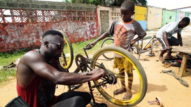 Odixco F Gongoar, owner of God Bless Bicycle Repair Center, repairs a bicycle as a trainee looks on in Paynesville, Liberia - Monday 24 May 2021